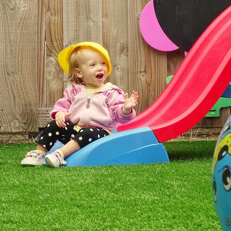 peuter-glijbaan-buitenspelen-kinderopvang-ark-oss » Kinderopvang & BSO in Oss Een vrolijke peuter glijdt van de glijbaan af in de buitenspeelruimte van Kindercentrum de Ark in Oss.