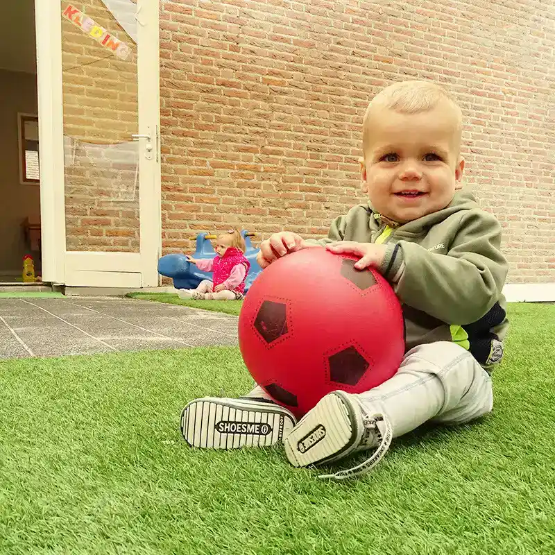 kind-met-rode-bal-gras-kinderopvang-ark-oss » Kinderopvang & BSO in Oss Een jong kind zit in het gras en houdt een grote rode bal vast tijdens het buitenspelen bij Kindercentrum de Ark in Oss.