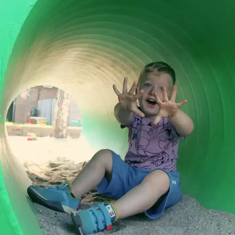 peuter-speelt-in-groene-kruiptunnel-ark-oss » Kinderopvang in Oss Een enthousiaste peuter kruipt door een groene tunnelbuis in de buitenspeelruimte van Kindercentrum de Ark in Oss.
