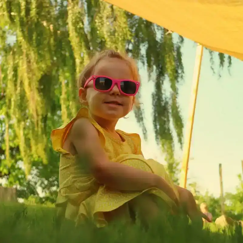 kind-met-zonnebril-in-gras-schaduw-ark-oss » Kinderopvang in Oss Een jong kind met een zonnebril op zit lekker in de schaduw in het gras bij Kindercentrum de Ark in Oss.