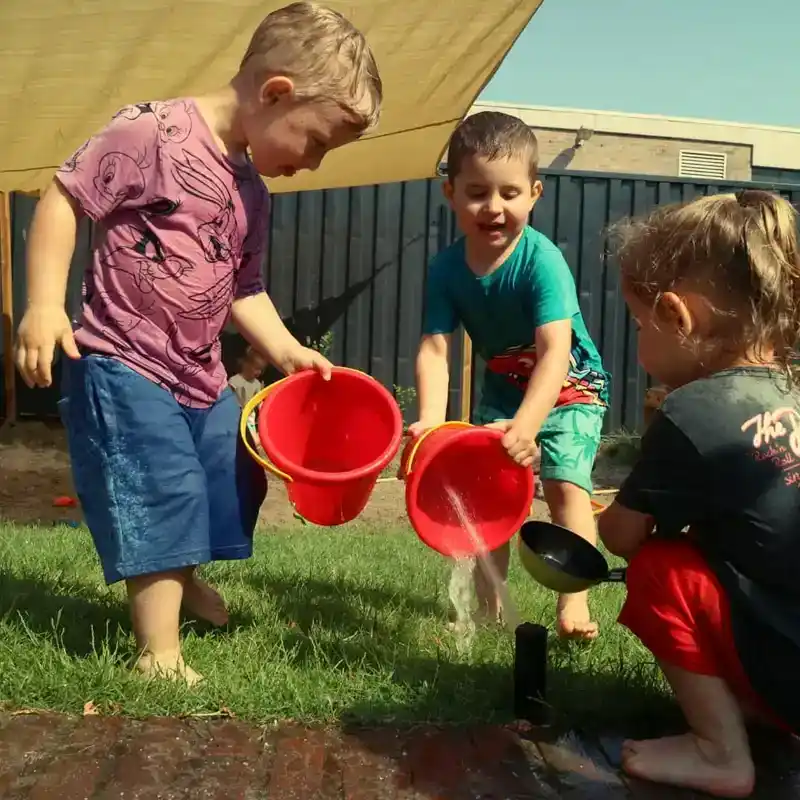 spelende-jongens-waterpret-rode-emmers-ark-oss » Kinderopvang in Oss Drie jongens spelen samen met water en rode emmers in het gras onder een schaduwdoek bij Kindercentrum de Ark in Oss.